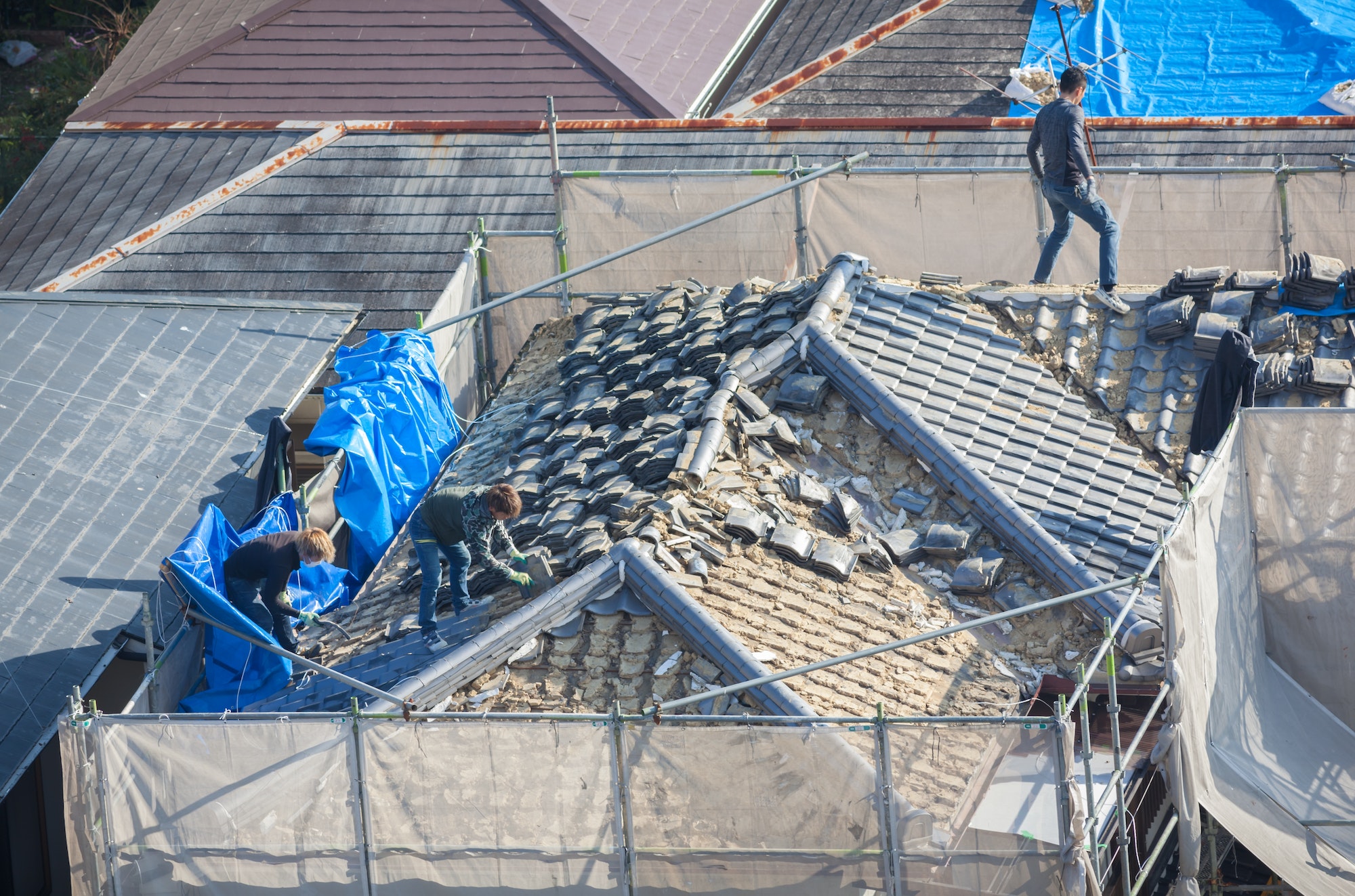 People working to tile a roof damaged by natural disaster